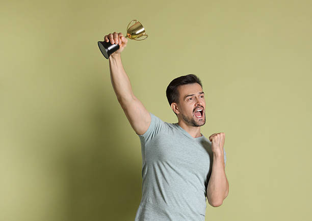 istock Emotional winner with golden trophy cup on pale olive background 2219433221