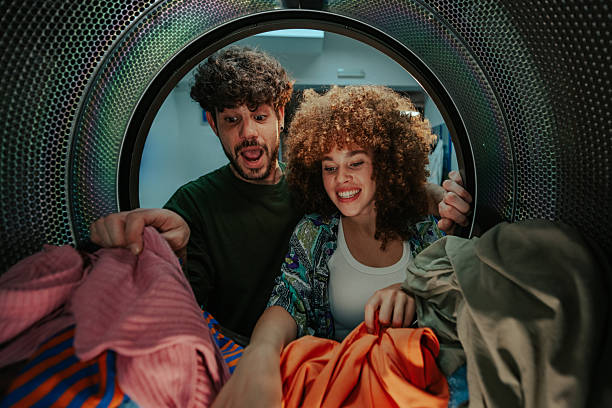 istock Young couple having fun looking inside laundromat dryer 2219437026