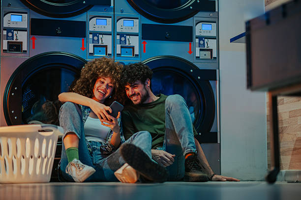 istock Young couple using smartphone while waiting for laundry at laundromat 2219437468