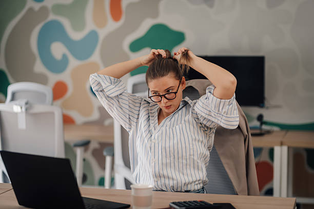 istock Office worker tying hair while working on laptop in modern office 2219440817