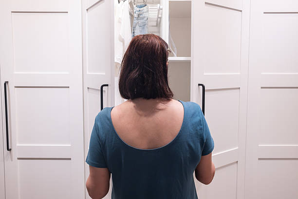 Middle aged woman opens wardrobe and chooses clothes for her husband. Neatly hung jackets, home routine, family care and organized domestic moment.