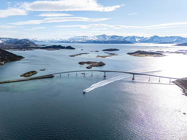 Boat sailing under a long bridge with stunning Arctic landscape. Serene ocean view, distant snow-capped mountains. Perfect for travel and nature enthusiasts showcasing Norway's beauty.