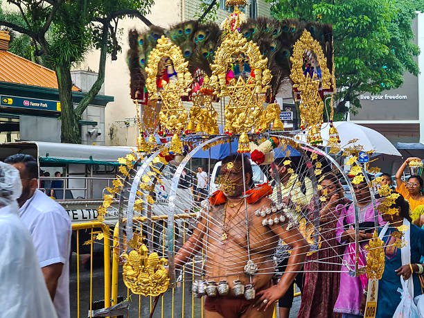 Singapore - February 5, 2023: Devotees participate in the colorful Thaipusam festival procession along the streets of Singapore.  The annual Hindu celebration includes rituals such as carrying kavadis, body piercings, and acts of devotion, drawing thousands of participants and spectators.\n\nThaipusam is a significant Hindu festival dedicated to Lord Murugan, celebrated mainly by the Tamil community. It symbolizes devotion, penance, and gratitude, with devotees often performing acts of physical endurance and carrying offerings to seek blessings or fulfill vows.