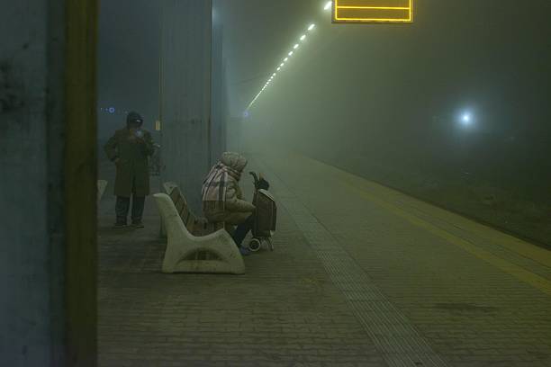 Sofia, Bulgaria - January 1, 2025: A misty evening scene at a railway station, where passengers huddle on benches waiting for their train, capturing the quiet, atmospheric mood of a cold, fog-filled night