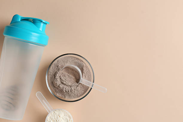 istock Protein powder in bowl, scoops and shaker on beige background, flat lay. Space for text 2219444116