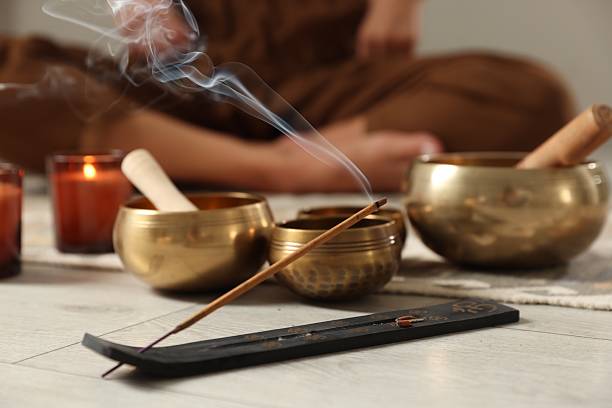 istock Incense stick smoldering in holder and tibetan singing bowls on floor, selective focus 2219445593