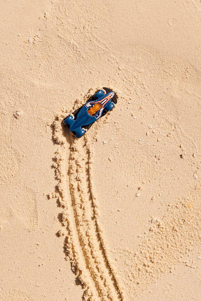 A small blue toy car leaves winding tire tracks on soft golden sand