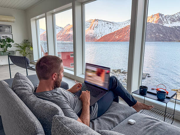 istock Man Relaxing on Sofa with Laptop Overlooking Scenic Mountain Lake 2219446198