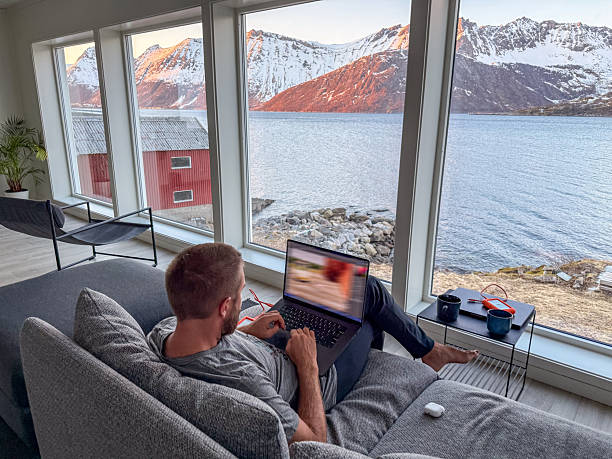 istock Man Relaxing on Sofa with Laptop Overlooking Scenic Mountain Lake 2219446200