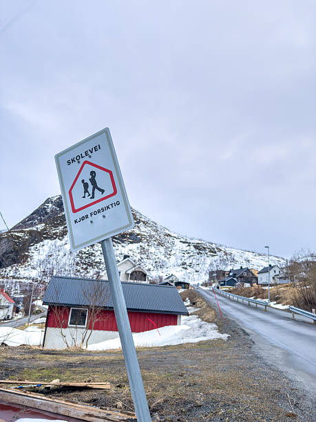 Longyearbyen, Svalbard and Jan Mayen Islands - September 20, 2024: A caution sign for snowmobile crossings stands prominently in Longyearbyen warning drivers as colorful buildings and rugged terrain form the backdrop under an overcast sky.