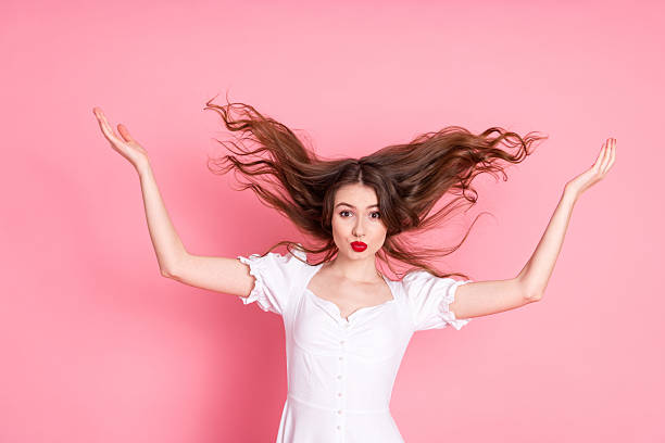 istock Young woman in a chic white dress posing with playful gestures on a vibrant pink background radiating confidence. 2219446708