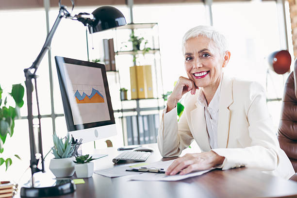 istock Elegant mature businesswoman posing confidently in a modern workspace with a computer showcasing a performance graph 2219450388