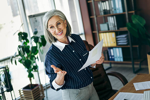 istock Confident mature businesswoman presenting documents in a modern office with elegant attire and professional demeanor 2219450734