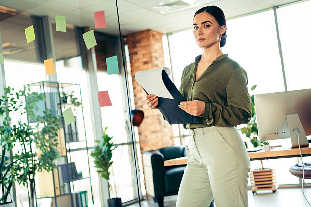 istock Confident young female professional holding folder, standing in modern office amid colorful notes, embodying expertise and ambition 2219452606