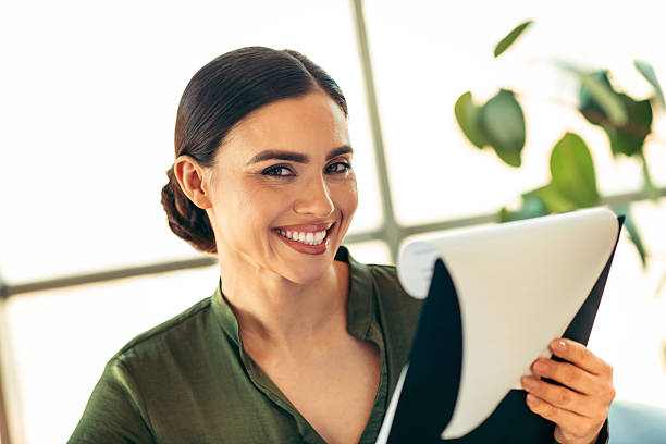 istock Confident businesswoman in elegant attire holding a document while smiling in a professional office setting 2219452643