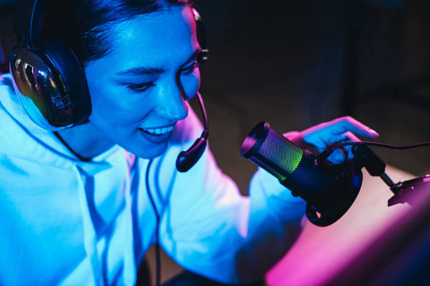 istock Young woman streaming as a content creator with a professional microphone and headset in a neon-lit gaming setup 2219457621