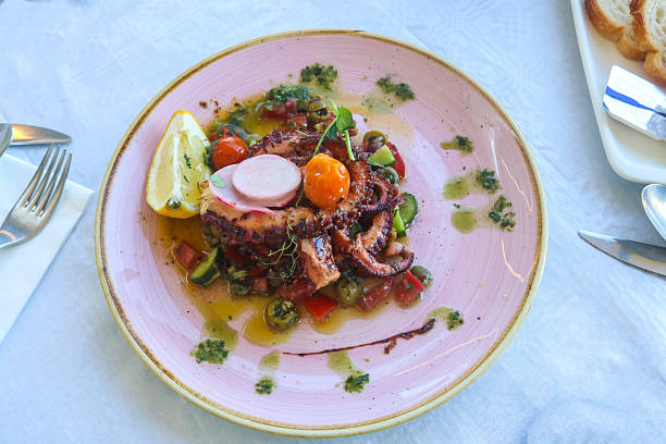 istock Delicious octopus dish served with lemon, vegetables and sauce in a restaurant. Top view 2219458937