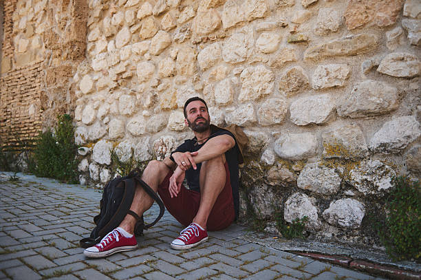 Man Resting Against Historical Stone Wall Amidst a Scenic Urban Setting