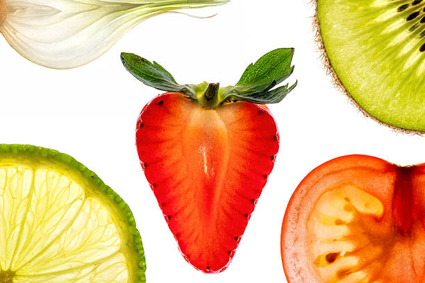 Backlit slices of various fruits and vegetables, including strawberry, kiwi, lime, tomato and onion, arranged on a white background, creating a vibrant and colorful composition