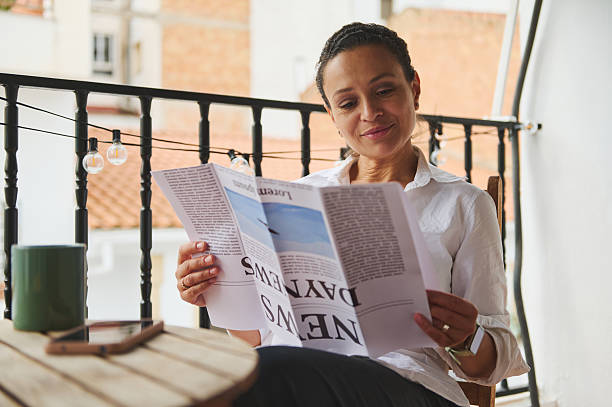istock Relaxed Woman Reading Newspaper On Balcony With Outdoor Setting 2219461577