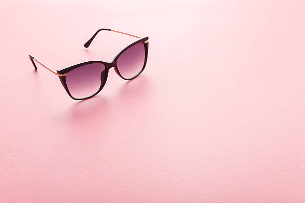 istock Female sunglasses with dark black plastic frame on light pink table background. Pastel color. Closeup. Empty place for text. 2219463117