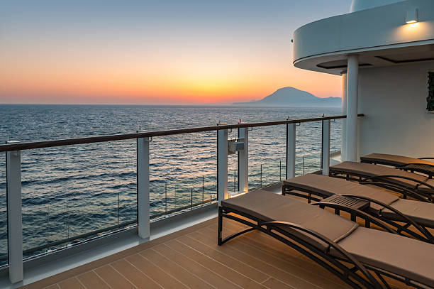 Travel photo with railing and sun loungers on deck of luxury cruise ship at sunset. Sun above the horizon, small waves at Mediterranean Sea.
