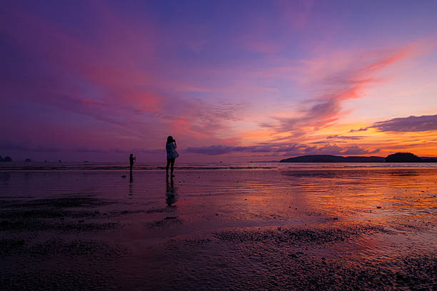 People stroll along the beach and watch the beautiful sunset.