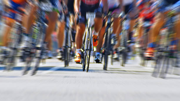 A dynamic medium shot captures a group of cyclists racing down a street, their motion blurred to convey speed and intensity. The focus on the center rider highlights the competitive nature of the event, emphasizing the thrill and energy of outdoor cycling.