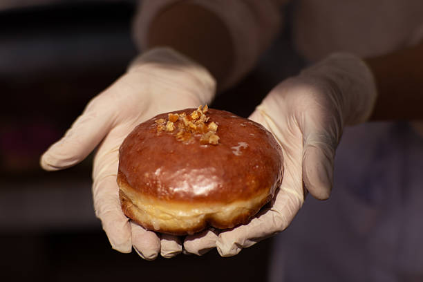 istock Close-up of a traditional Polish doughnut held by gloved hands. 2219476466