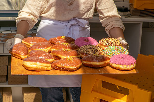 istock Person holding a wooden tray with assorted glazed donuts at a bakery 2219476486