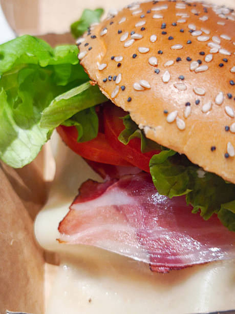 istock Close up gourmet burger highlighting crispy lettuce, juicy tomato, savory bacon, melted cheese on sesame seed bun, representing culinary excellence 2219478675