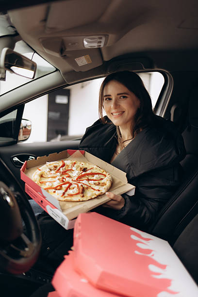 istock Smiling Woman Holding Pizza Box While Seated Inside a Car 2219482034