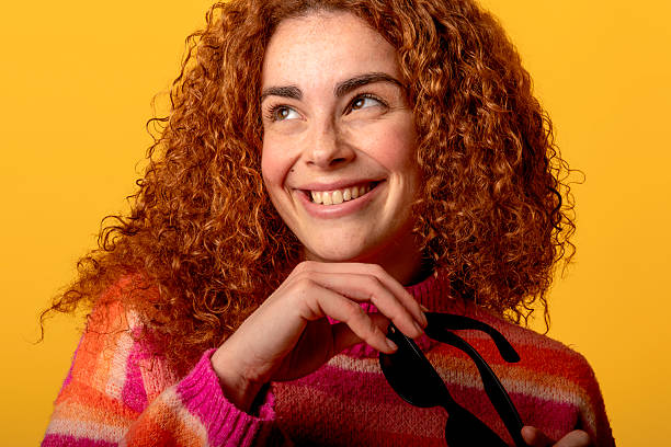 istock Redhead model smiling and holding sunglasses in studio with yellow background 2219482159