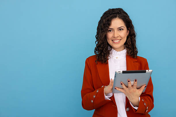 istock Professional businesswoman working on digital tablet, smiling confidently against blue backdrop 2219482669