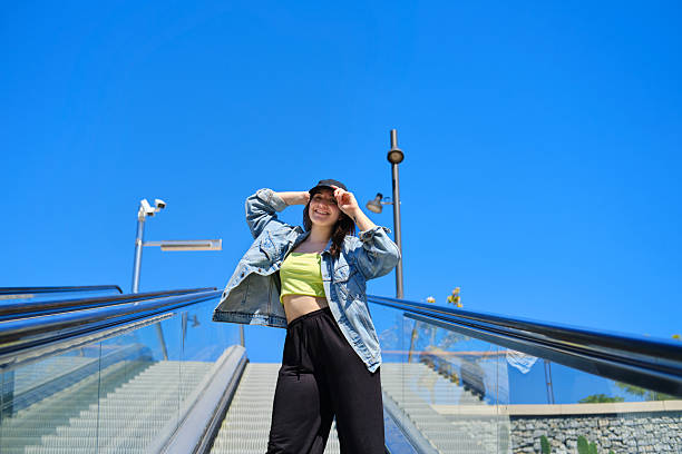 istock Young stylish woman posing on escalator against blue sky 2219485238