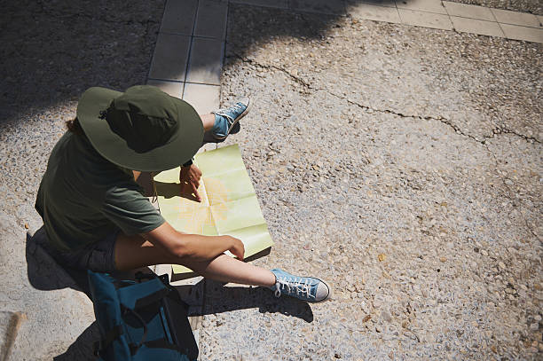 An adventurer consults a map in a sunny historic town, showcasing exploration, planning, and outdoor travel amidst medieval surroundings with a backdrop of natural beauty.