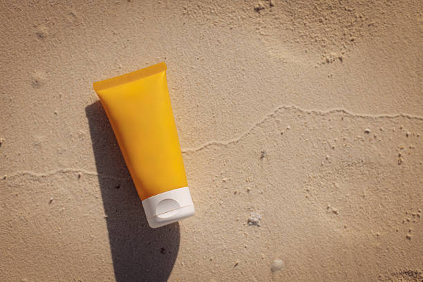 A vibrant yellow sunscreen tube rests on golden sand under bright sunlight, reflecting a sunny beach setting, ideal for summer skincare and sun protection