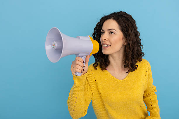 istock Female activist shouting through megaphone, raising voice against blue backdrop 2219488727