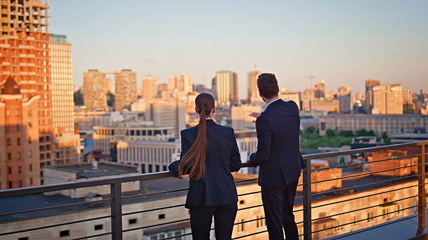 istock Office colleagues looking cityscape view on sunset rooftop. Two coworkers 2219489359