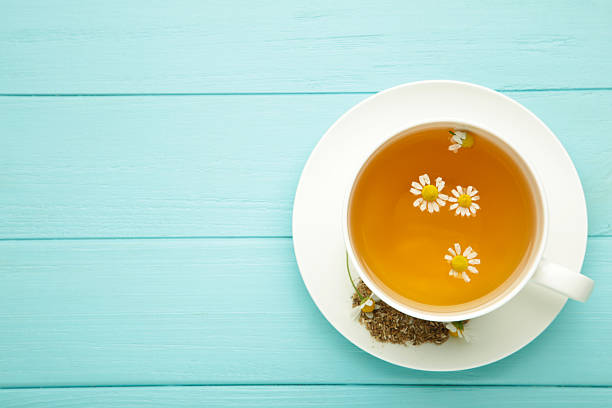 istock Aromatic herbal tea in white cup and chamomiles on blue background. 2219492042