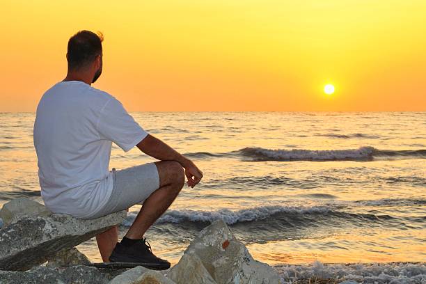 istock Man sitting on rocks and watching sunset over the sea 2219500183