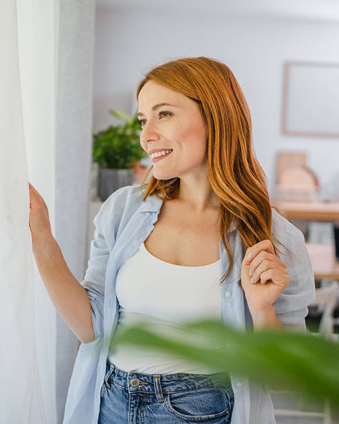 istock Portrait of redhead smile while look through window at home 2219502123