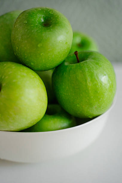 istock Bright green apples on a white surface, emphasizing their freshness and beauty. The healthy fruit looks inviting and creates a refreshing visual appeal. 2219503349