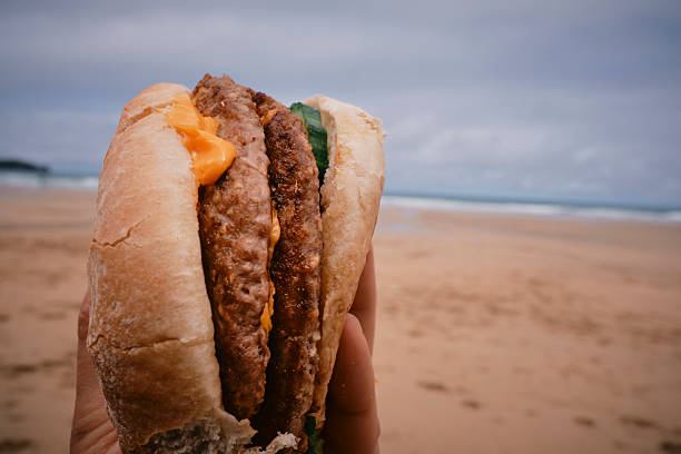 POV of a hand holding a cheese burger at the beach. Beach holiday food.