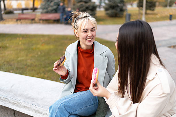 istock Two young women smiling and eating donuts in a park 2219506641