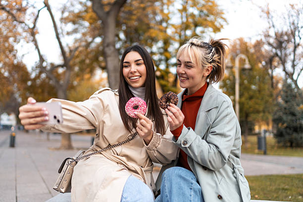 istock Two young women taking a selfie while eating donuts in a park 2219506713