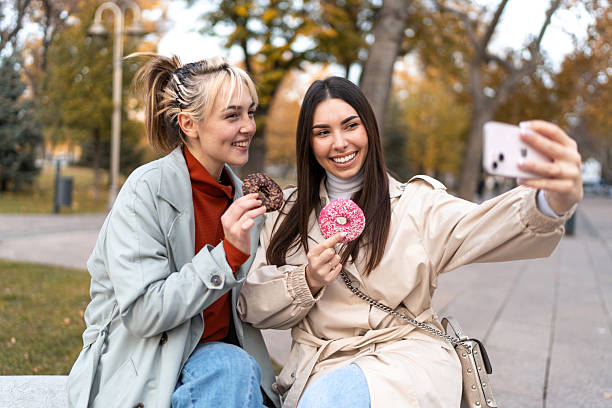 istock Two young women taking a selfie while eating donuts in a park 2219506715