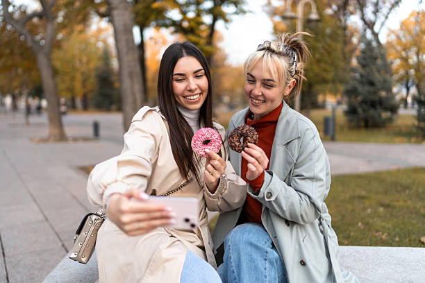 istock Two young women taking a selfie while eating donuts in a park 2219506730