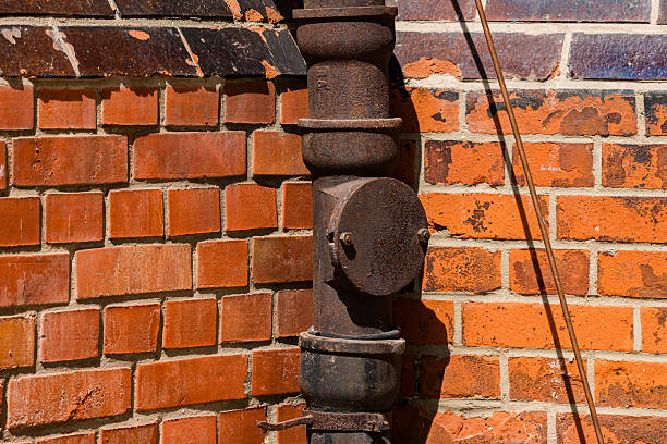 A close-up view of a rusty pipe mounted on a textured orange brick wall. The setting reflects an urban environment, showcasing signs of aging and industrial charm.