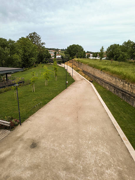 istock Inviting park path leading to distant homes under a cloudy sky. Ideal for depicting journey, lifestyle, recreation, or urban planning concepts. Serene, calm, nature. 2219512969